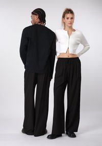 Sort langærmet skjorte, cropped hvid ribbet cardigan, sorte bukser med brede ben og striber samt platformsko, set bagfra.