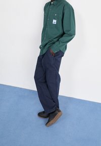 Grön skjorta med knappar och bröstficka, kombinerad med marinblå cargobyxor. Svarta skor med texturerade sulor. Slät tyg, avslappnad passform.