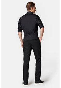 Czarna dopasowana koszula z wysokim kołnierzem, regulowanym zapięciem z tyłu i podwiniętymi rękawami. Połączona z wąskimi czarnymi spodniami i teksturowanymi trampkami.