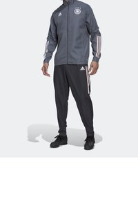 Adidas grå træningsdragt bestående af en zip-up jakke med logo og tre hvide striber, parret med sorte bukser prydet med lyserøde striber.