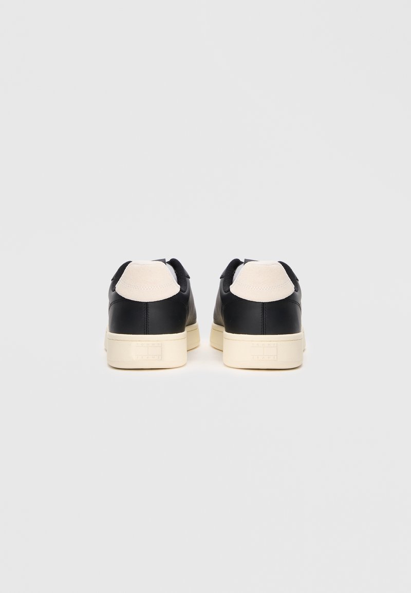 Black leather sneakers with cream accents, featuring a smooth surface and a textured heel tab. Chunky cream outsole with branding detail.