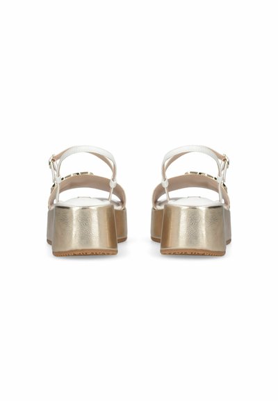 Sandales en cuir blanc avec talons compensés métalliques dorés, brides de cheville et fermetures à boucle à l'arrière, vues de dos sur fond blanc.
