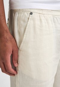 Linnedragter med snore i en lys beige farve, med en afslappet pasform, sideskaber og en knapdetalje på taljen.