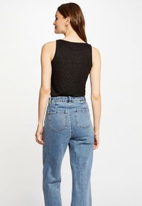 Black sleeveless top made of soft, glittery fabric, paired with high-waisted light blue denim jeans featuring back pockets and a relaxed fit.