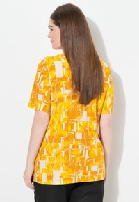 Chemise jaune à manches courtes arborant un motif géométrique avec des formes abstraites et des motifs solaires, fabriquée en tissu léger.