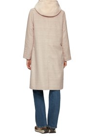 Manteau à carreaux rose clair avec une capuche douce et pelucheuse. Il possède des manches longues et tombe juste au-dessus du genou, associé à un jean bleu et des baskets.