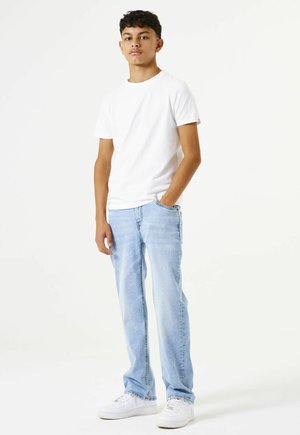 T-shirt en coton blanc, jean en denim bleu clair et baskets blanches ; coupe décontractée avec un design simple, col cheminée et poches latérales.