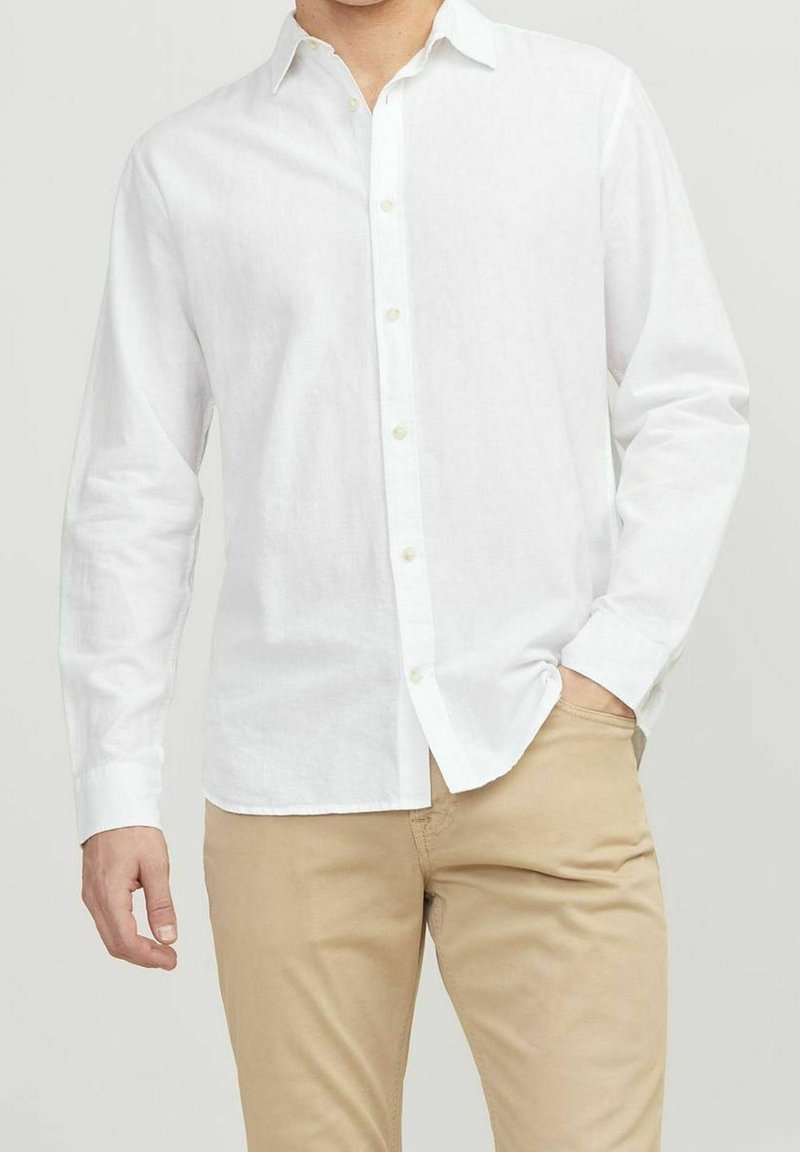 Camisa de lino blanca de botones, con mangas largas, cuello y una textura sutil. Combinada con pantalones beige claros.