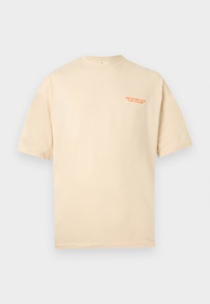 Camiseta beige de manga corta con un pequeño texto naranja en el lado izquierdo del pecho que dice "THE WURST CLUB Salchichas y Relájate."