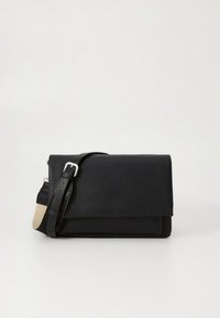 Črna teksturirana usnjena torbica čez ramo z nastavljivim trakom, ki ima srebrno zaponko in bež tkaninski detajl na belem ozadju.