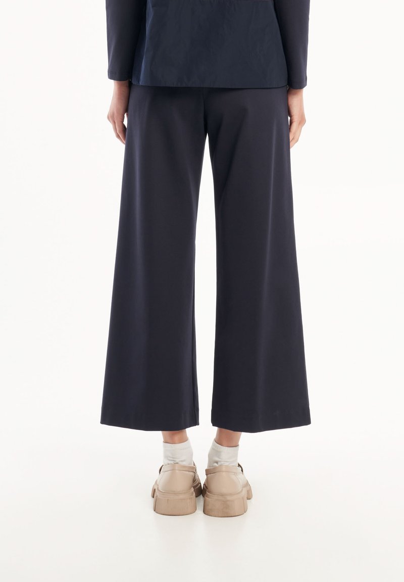 Pantaloni a gamba larga blu navy realizzati in tessuto morbido, con vita alta e vestibilità rilassata, abbinati a scarpe e calzini chiari.