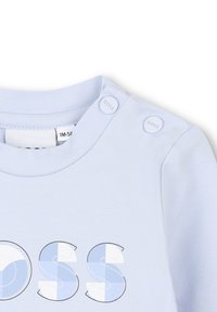 Jasnoniebieski bawełniany sweter z okrągłym dekoltem, dwoma guzikami na ramieniu oraz graficznym logo "BOSS" w różnych odcieniach niebieskiego.