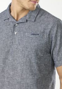 Grå kortärmad polo skjorta i strukturtyg, med knapplåst krage och en liten "SEASIDE"-logotyp på bröstfickan.