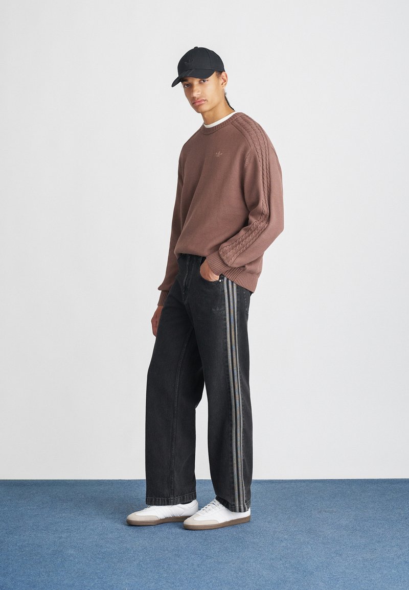 Brown knit sweater with cable-knit detail on sleeves, paired with black wide-leg jeans featuring side stripes and white sneakers.