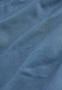 Tejido texturizado en un tono azul profundo, que muestra un patrón tejido con aristas visibles y suaves pliegues que caen.