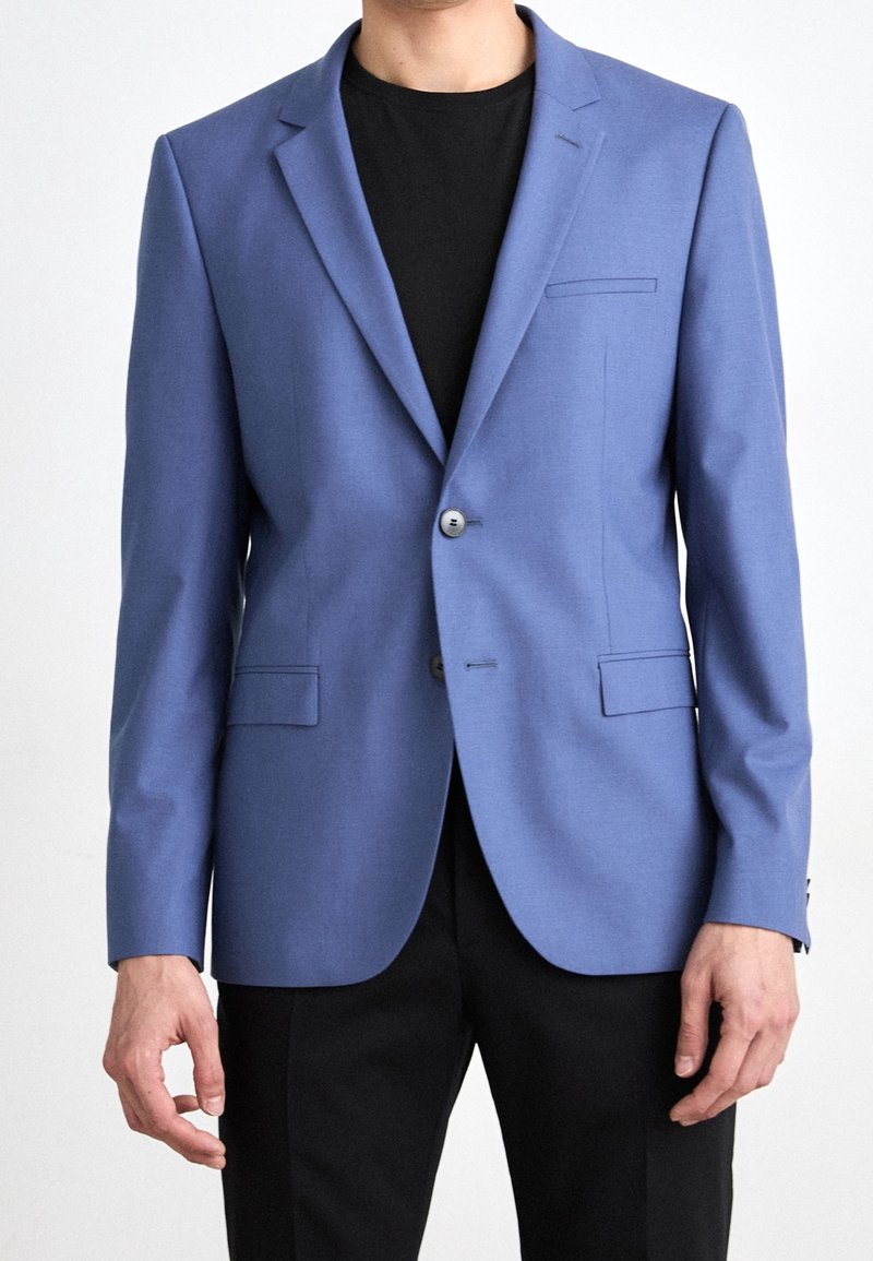 Modrý blazer vyrobený z hladké tkaniny, s jedním knoflíkem, s klopami, dvěma předními kapsami a štíhlým střihem.