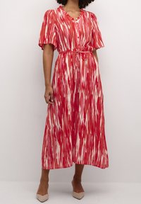 Robe maxi à motifs rouges et roses avec manches courtes bouffantes, encolure en V, boutonnage devant, et détail de taille nouée. Tissu lisse, design fluide.