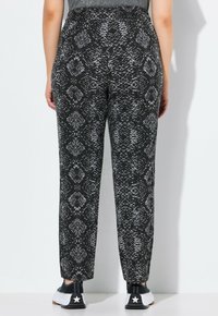 Pantalons noirs et gris à motifs avec un design imprimé serpent, présentant une coupe fuselée et un tissu doux. Portés avec des baskets noires.
