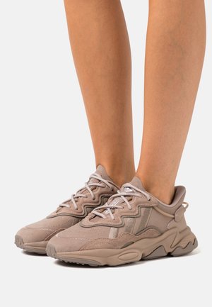 Zapatillas deportivas beige con parte superior de ante texturizado, diseño en capas, acentos reflectantes y suela acolchada. Incluye cordones y tirador.