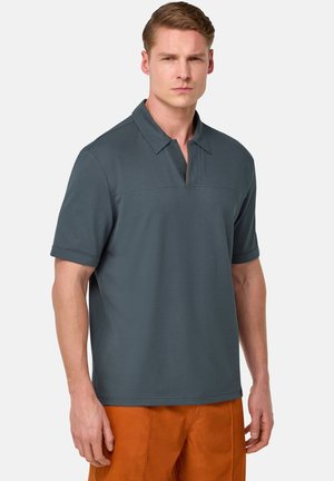 Dunkelgraues Polohemd mit kurzem Kragen und halber Knopfleiste, kombiniert mit orangefarbener Hose. Der Stoff wirkt glatt und leicht.