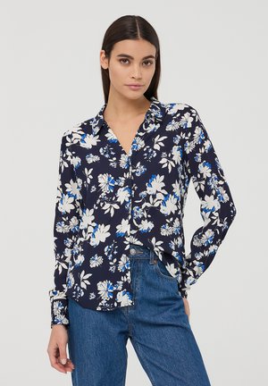 Blusa floreale navy con fiori bianchi e blu, con bottoni frontali e maniche lunghe; abbinata a jeans in denim a vita alta.