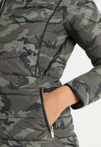 Grøn camouflage pufferjakke med vandret quiltet mønster, sidelommer med lynlås og sorte lynlåsdetaljer på fronten og lommerne.