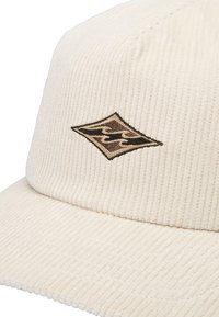 Corduroy kasket i off-white, med et struktureret ribbet design. Et brunt broderet diamantlogo pryder forsiden.