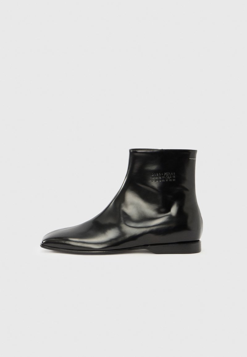 Sort ankelstøvle med en skinnende, glat læderfinish. Spids tå, lav stacket hæl, minimalistisk design og præget logodetalje på siden.