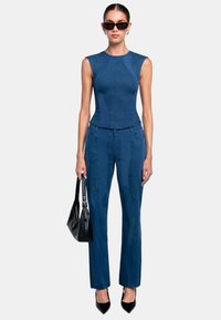 Dark blue sleeveless top with textured design, paired with matching fitted pants featuring vertical accents. Model holds a black handbag.