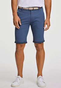 Shorts chino blu navy con orli risvoltati, realizzati in un tessuto testurizzato e dotati di una cintura intrecciata. Abbinati a sneakers bianche su uno sfondo neutro.