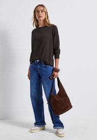 Dunkelbraunes Langarmoberteil, blaue hochgeschnittene Jeans, weiße Turnschuhe und eine braune Wildleder-Schultertasche. Glatter Stoff und lockere Passform.