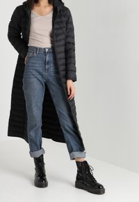 Abrigo acolchado negro con capucha, de largo, llevado sobre una camiseta de canalé beige y jeans azul de talle alto; completado con botas negras con cordones.