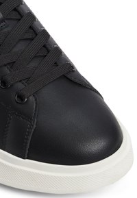 Černé kožené tenisky s kulatou špičkou, plochou bílou gumovou podrážkou a černými tkaničkami. Mají strukturovaný povrch a zesílené švy.