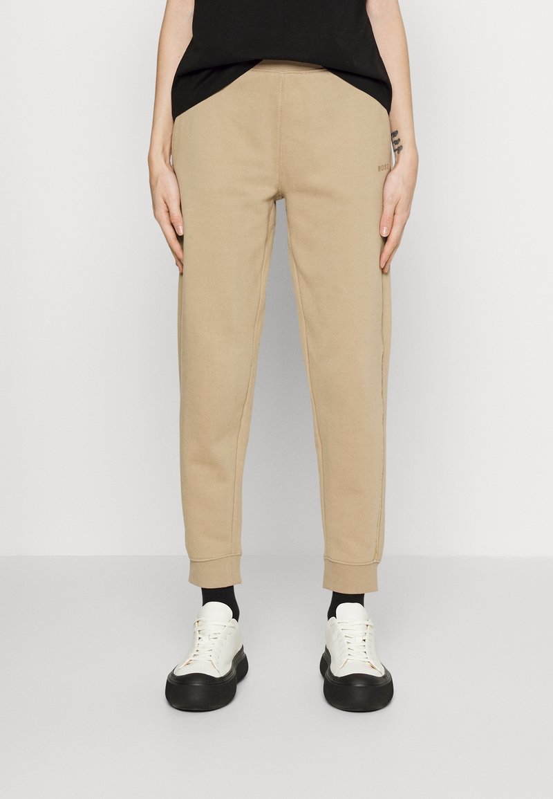 Beige Jogginghose mit schmal zulaufendem Schnitt, ausgestattet mit Seitentaschen und gerippten Bündchen, kombiniert mit weißen Sneakers und schwarzen Socken.
