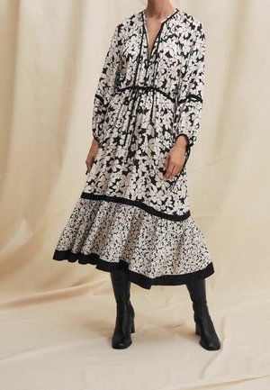 Mekko, jossa on pitkät hihat ja mustavalkoinen kukkakuvio, vyötärö kiristettynä, kerroksittainen helma ja musta reunus. Yhdistetty polvenkorkuisiin mustiin saappaisiin.