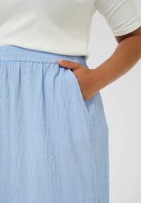 Light blue, textured skirt with a gathered waistband and side pockets, paired with a white, fitted top.