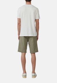 T-shirt blanche à manches courtes, shorts olive, baskets beiges. Design simple, tissu doux, coupe décontractée, sans motifs ni embellissements.