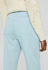 Pantalon taille haute bleu clair avec une texture lisse et des poches latérales discrètes, associé à un pull en maille épaisse couleur crème.