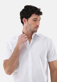 Weißes kurzärmliges Hemd mit Knopfleiste und dezentem Karomuster, ausgestattet mit einem spitzen Kragen und glatter Stofftextur.