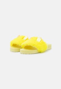 Yellow fluffy slide sandals featuring textured fur upper with shiny gold ears, flat rubber sole, and wide open toe design.