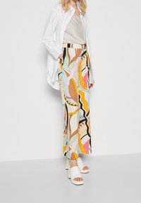 Flerfärgade abstrakta mönstrade vida byxor, tillverkade av lätt tyg, i kombination med en ljus topp och vita klacksandaler med blockklack.