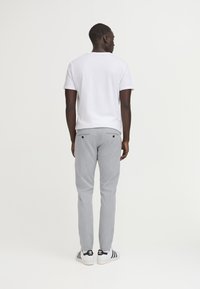 Hvid kortærmet t-shirt parret med lysegrå, lige ben bukser. Bukserne har to baglommer med sorte knapper og et diskret mønster.