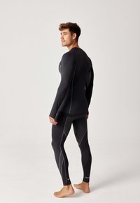 Zwarte sportoutfit bestaande uit een aansluitend T-shirt met lange mouwen en leggings, met contrasterende textuurpanelen en witte stiksels.