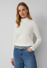 Witte lange mouwen coltrui met een soepele textuur, gecombineerd met blauwe jeans en een gestreepte riem met een lichtblauw en grijs luipaardpatroon.