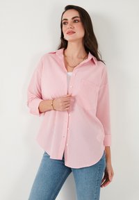 Red and white striped button-up shirt with a relaxed fit, long sleeves, a chest pocket, and a curved hem, paired with light blue jeans.