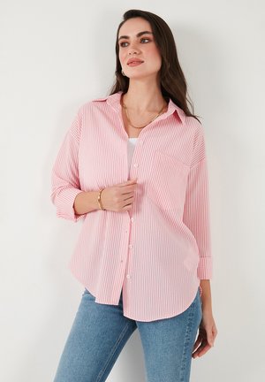 Red and white striped button-up shirt with a relaxed fit, long sleeves, a chest pocket, and a curved hem, paired with light blue jeans.