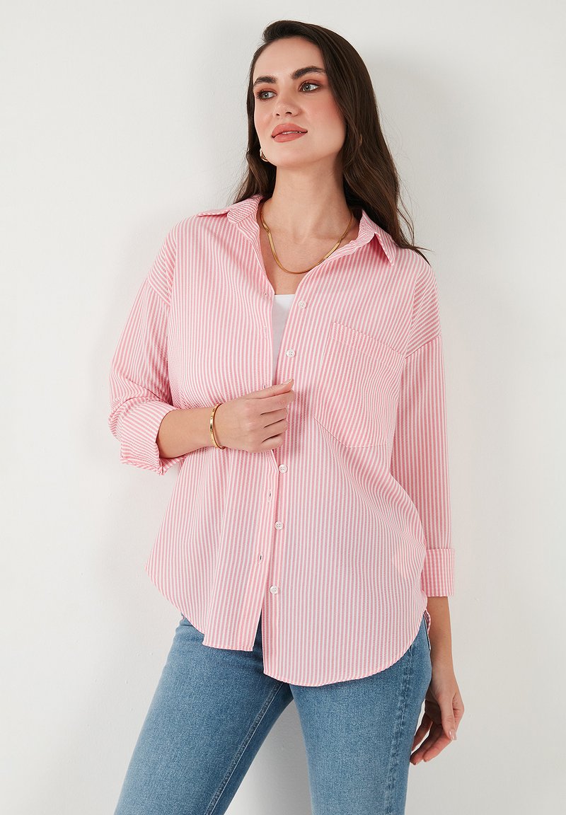 Red and white striped button-up shirt with a relaxed fit, long sleeves, a chest pocket, and a curved hem, paired with light blue jeans.