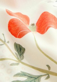 Fiore rosso con stelo e foglie verdi su uno sfondo di tessuto color crema chiaro. Il fiore presenta petali dettagliati, creando un aspetto morbido e testurizzato.