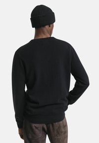 Maglione nero a maglia con orlo e polsini a coste, caratterizzato da un colletto rotondo e una texture liscia. Indossato con un berretto nero coordinato.