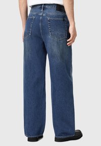 Siniset farkut rentoa istuvuutta, jossa on korkea vyötärö, leveät lahkeet, kaksi takataskua ja hienovarainen haalistunut pinta.